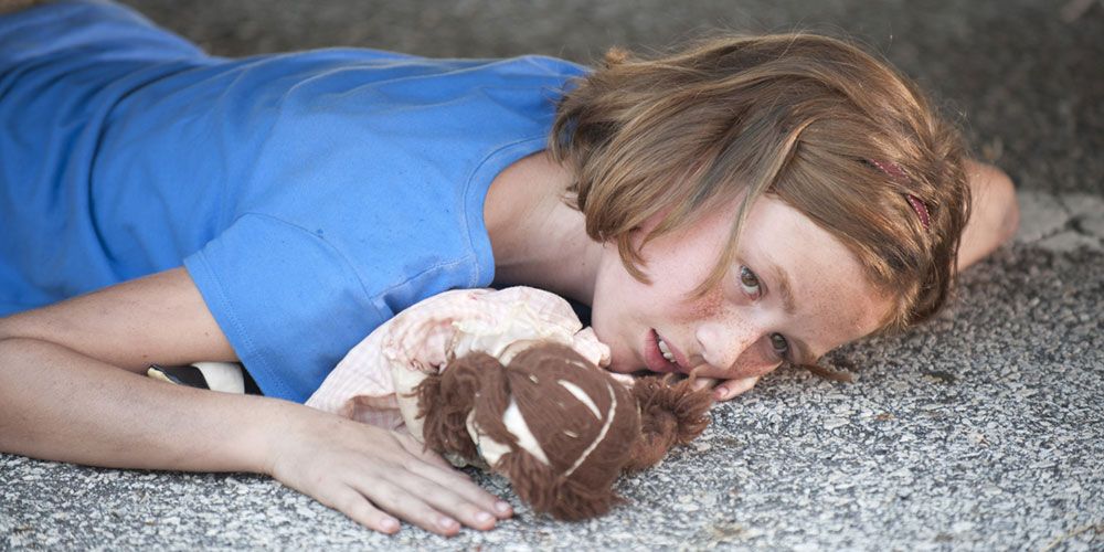 Sophia Peletier in The Walking Dead lying on the ground with a stuffed animal.