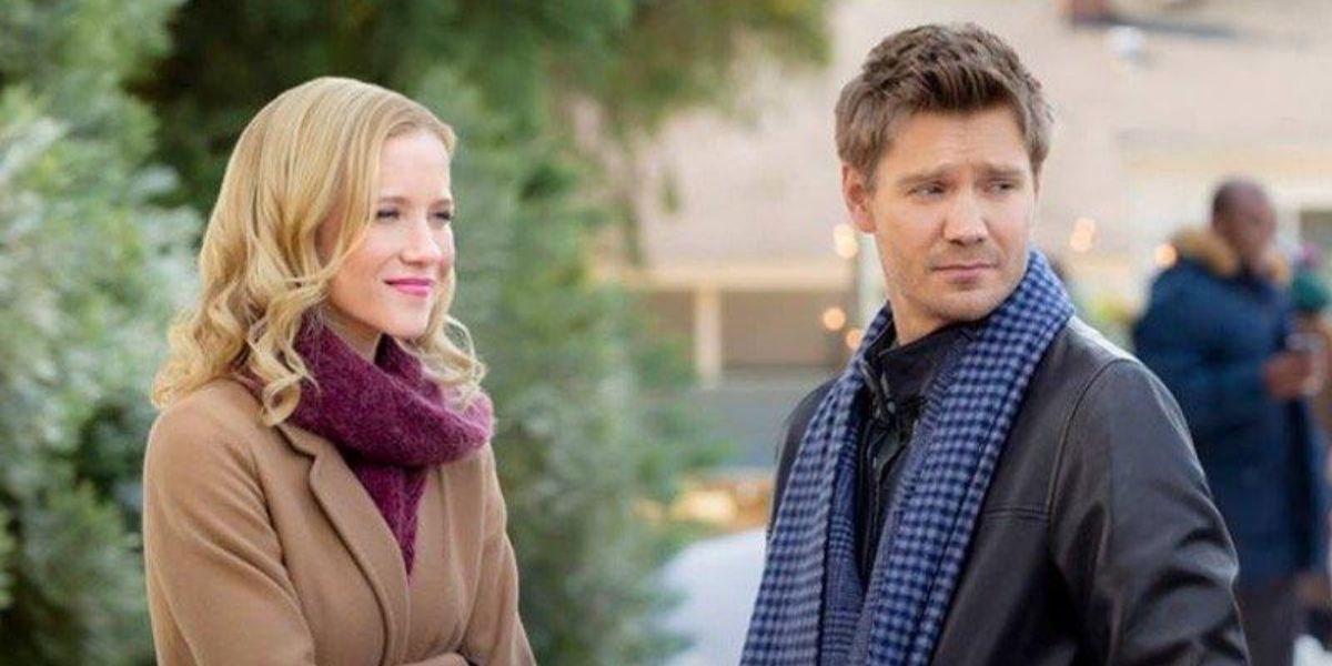 Two characters in a Hallmark Christmas movie standing outside by the trees