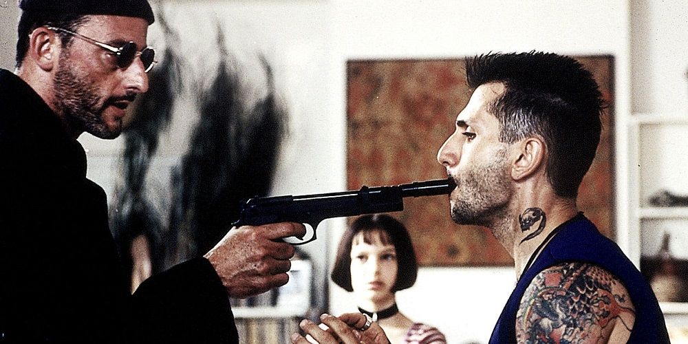 Leon holding a silencer to an enemy’s mouth as Mathilda watches