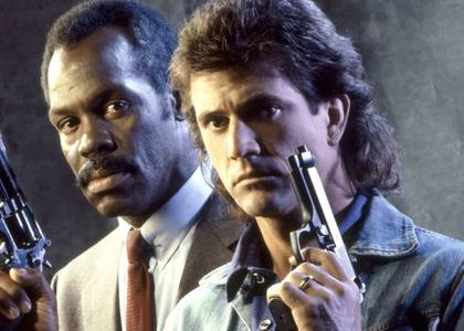 Mel Gibson as Riggs and Danny Glover as Murtaugh holding up guns in Lethal Weapon