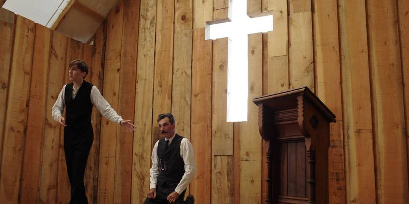 Daniel Plainview (Daniel Day-Lewis) kneeling while Eli Sunday (Paul Dano) prays over him in a church in There Will Be Blood.