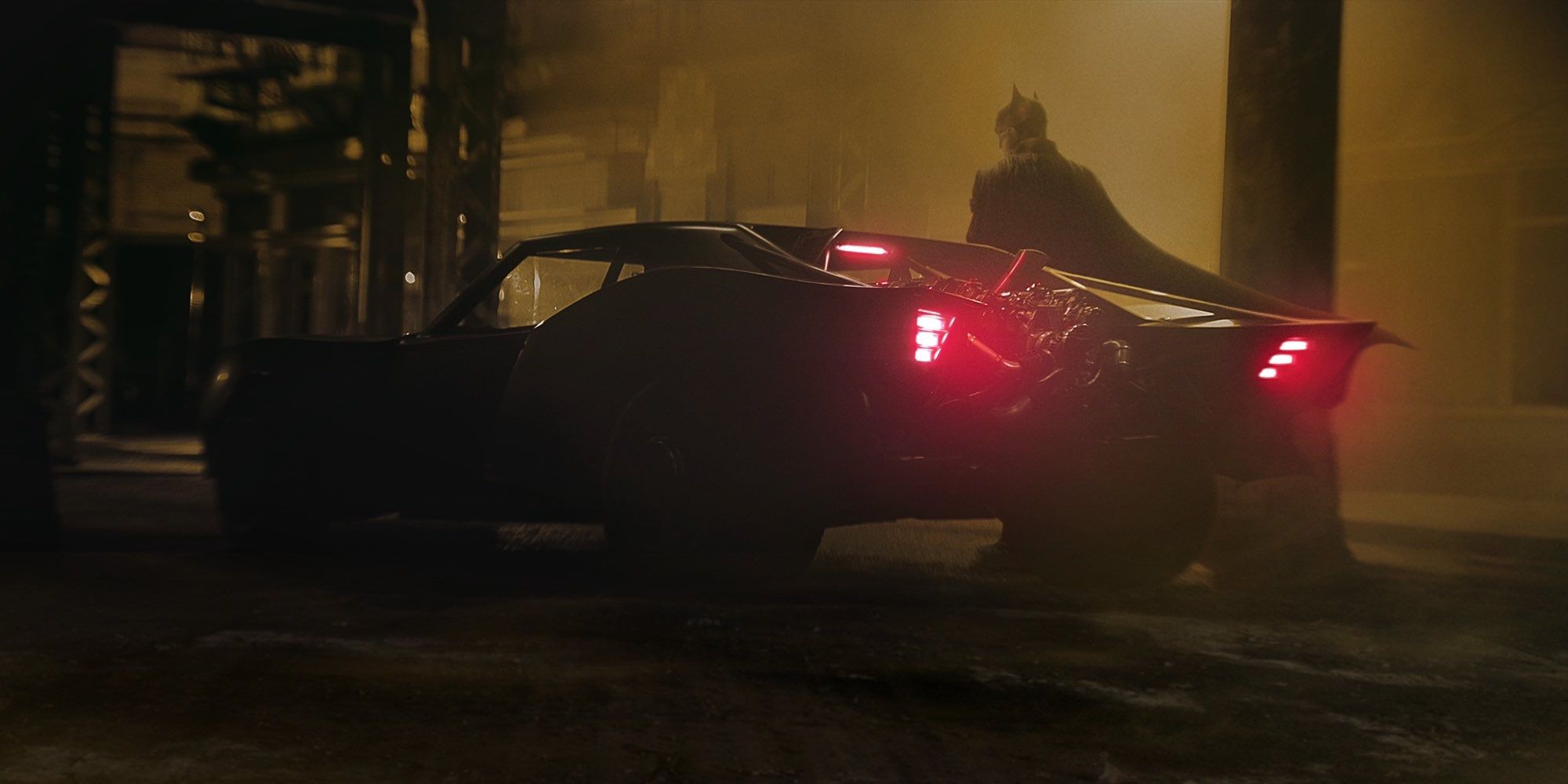 Robert Pattinson stands next to the Batmobile in The Batman