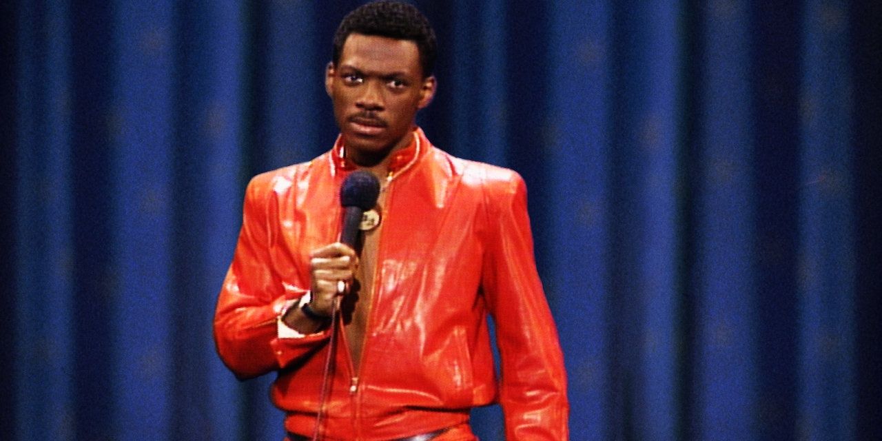 Eddie Murphy in his red jacket holding the mic in the Delirious comedy special