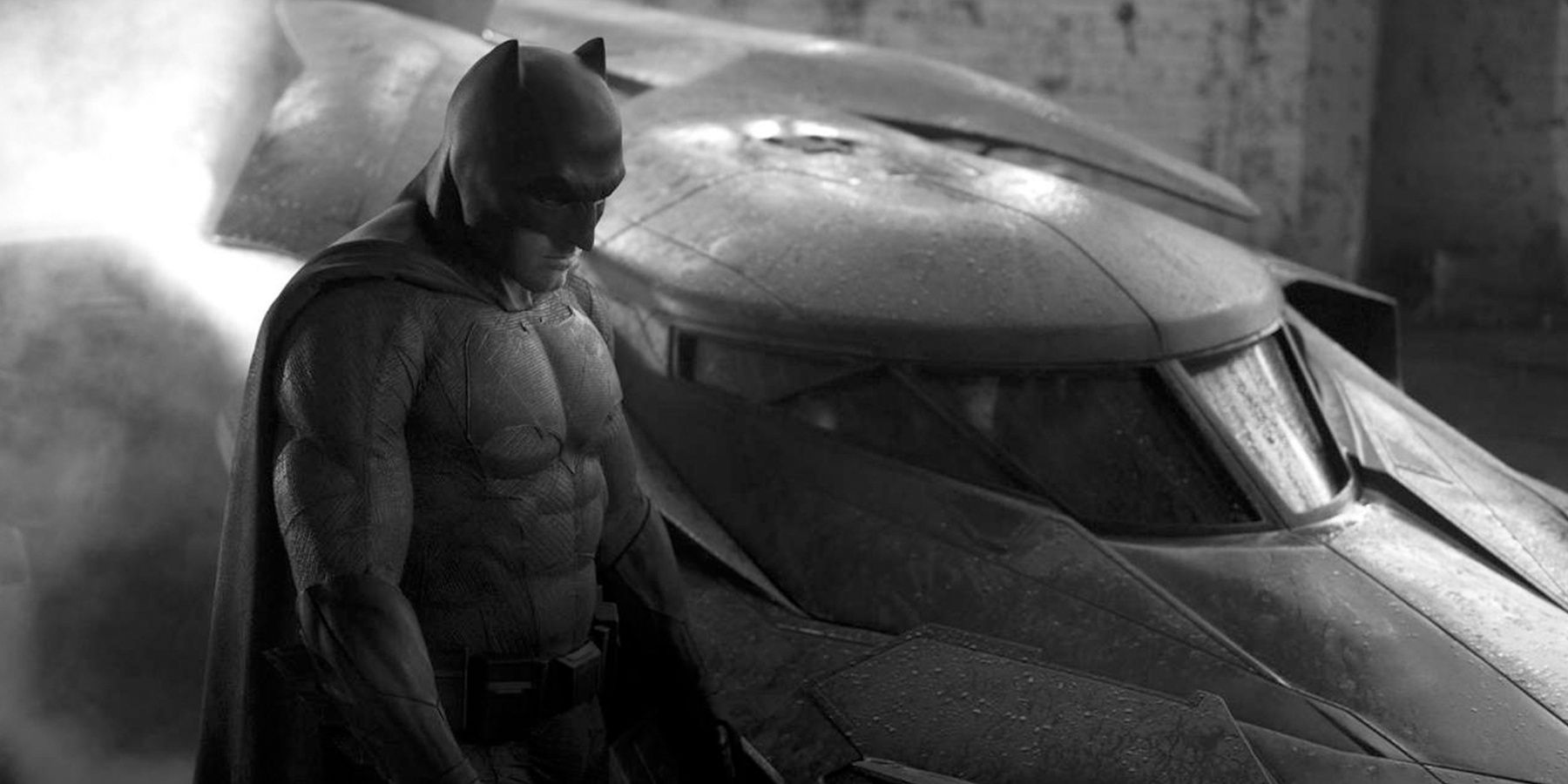 Ben Affleck as Batman next to the Batmobile in black and white