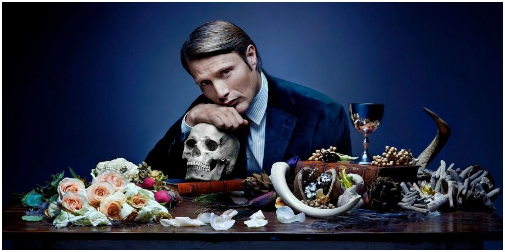 Mads Mikkelsen as Hannibal Lecter at the table resting on a skull