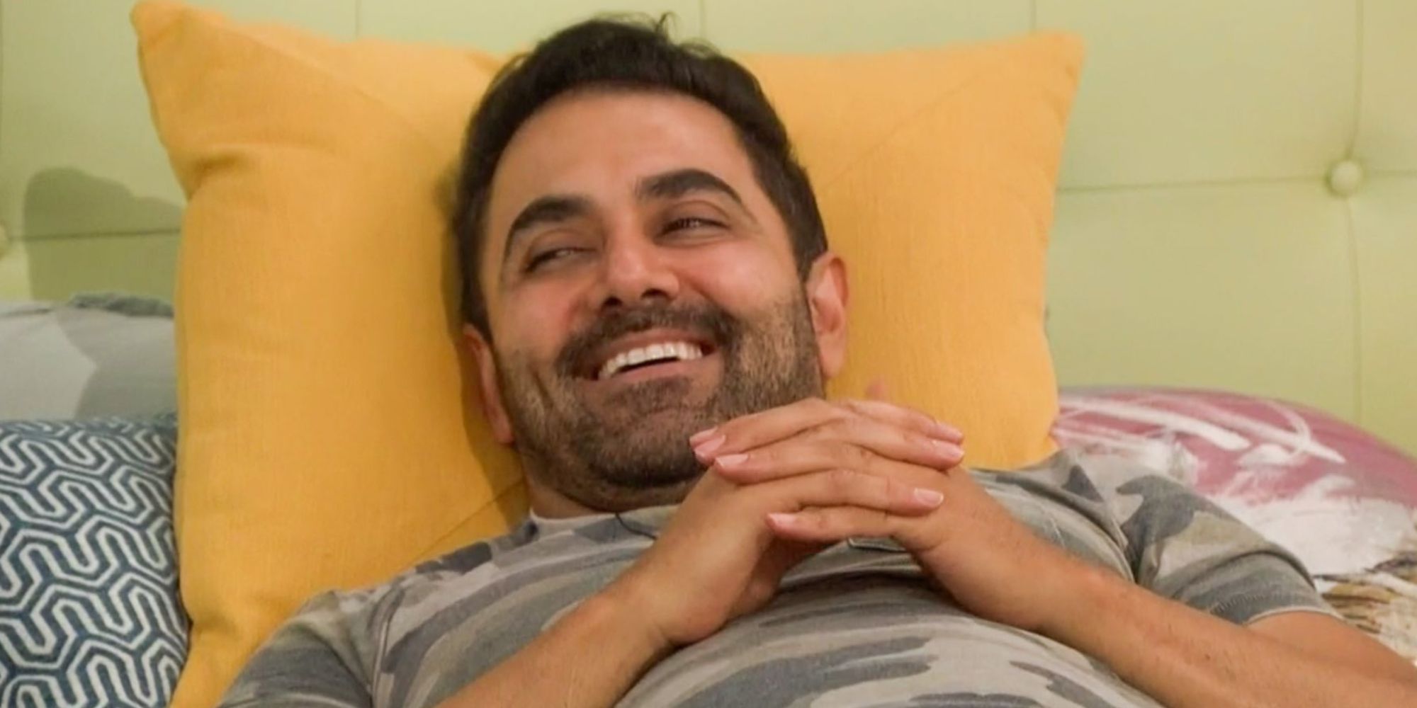 Kaysar living on the bed with his hands clasped together smiling and laughing