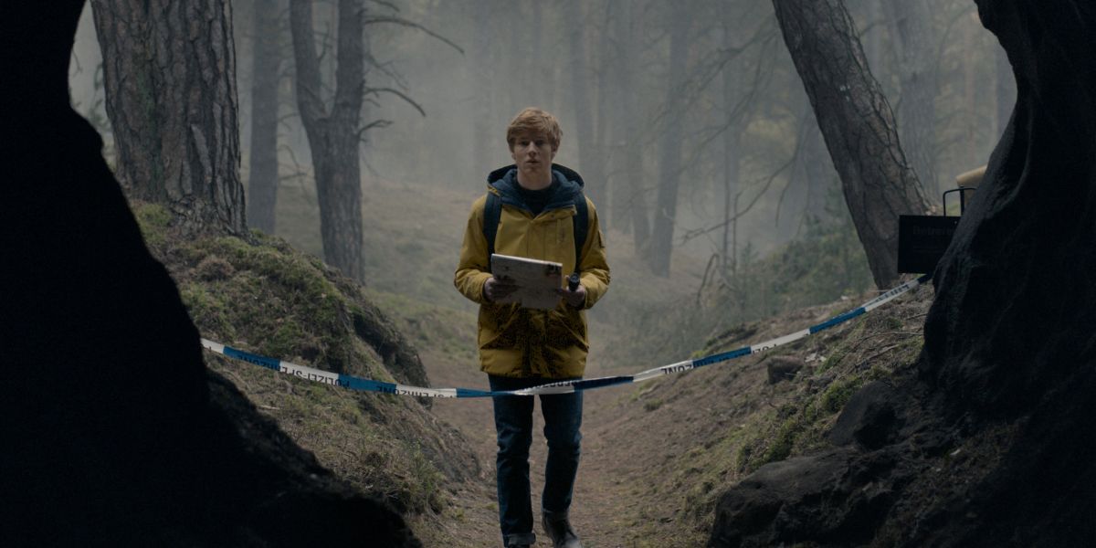 A young man in a yellow jacket stands at the mouth of a cave in Dark 