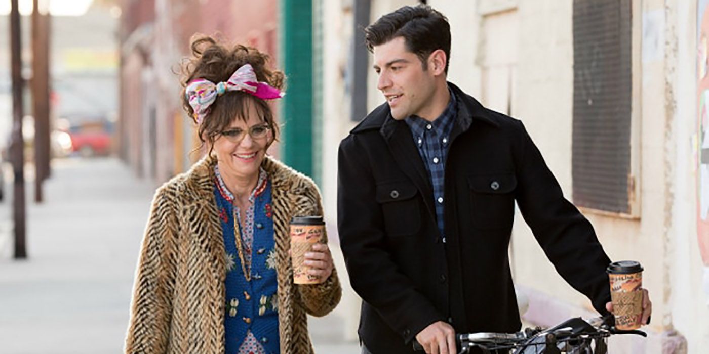 Sally Field is holding a coffee and Max Greenfield is walking his bike as the two are walking next to one another. 