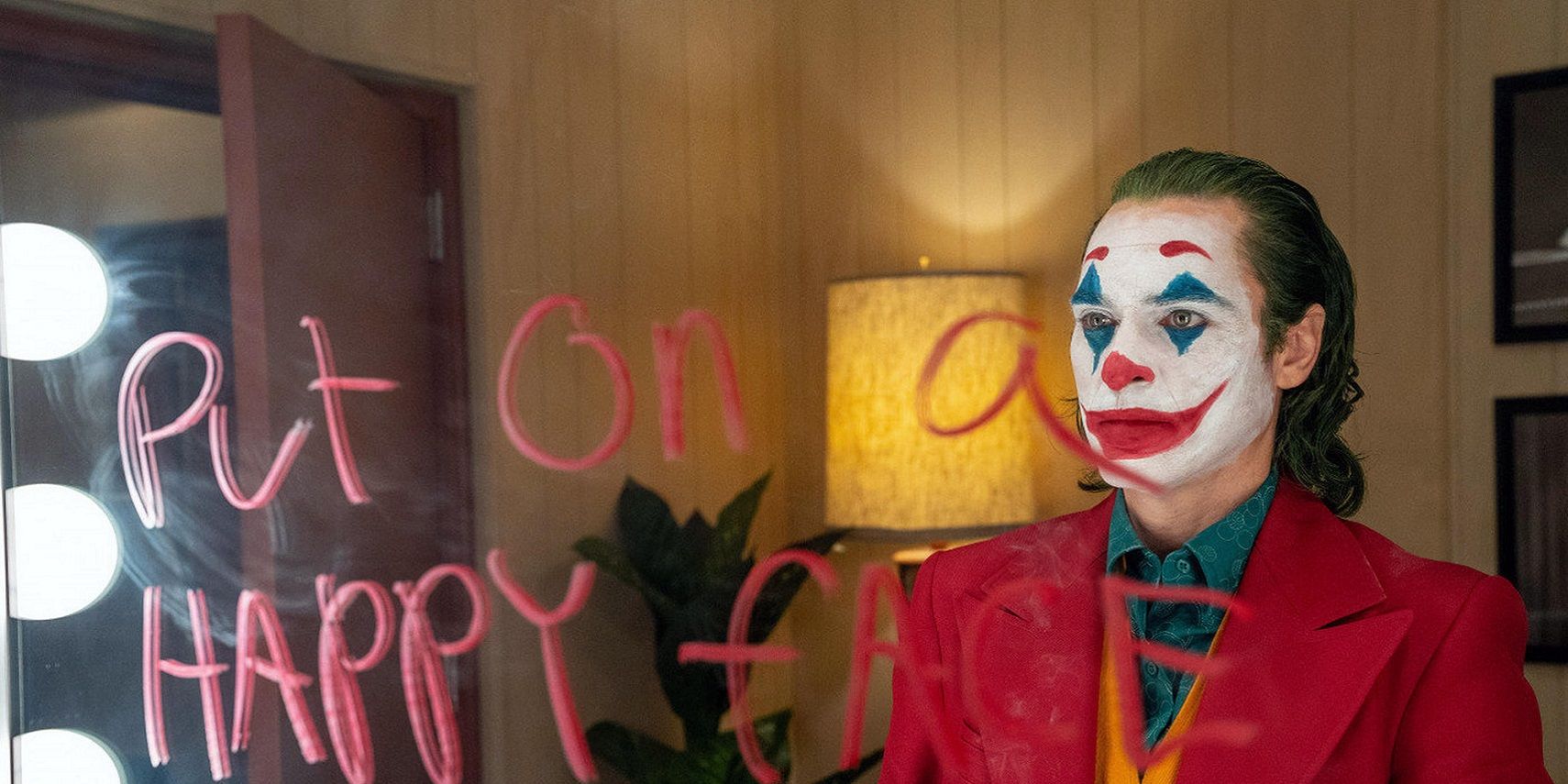 Arthur looks in the mirror wearing clown make up in Joker