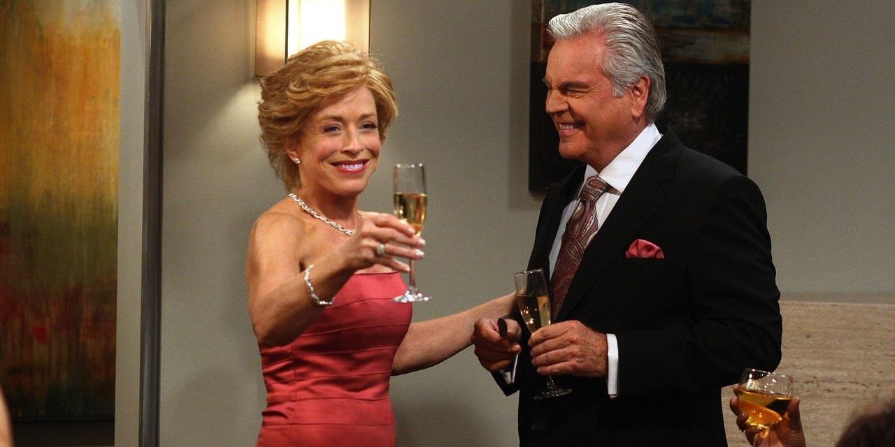 Evelyn in a pink strapless gown raising a glass as Teddy looks on and smiles in Two and a half men