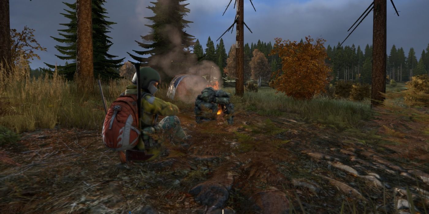 A player in DayZ sitting next to a campfire at dusk