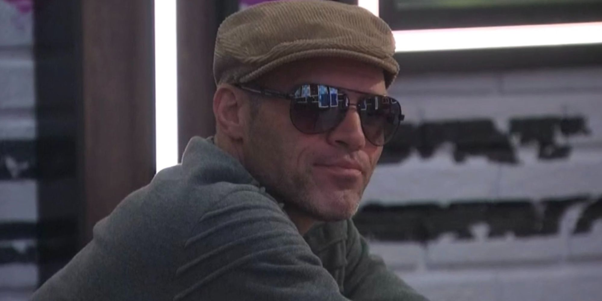 Enzo sitting with a hat and dark sunglasses in a scene from Big Brother 22.