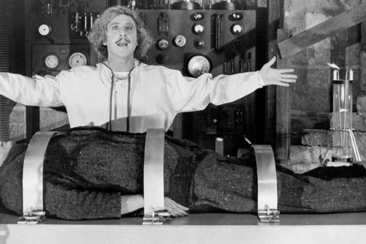 Frederick Frankenstein with his arms open with the monster on his operating table in Young Frankenstein