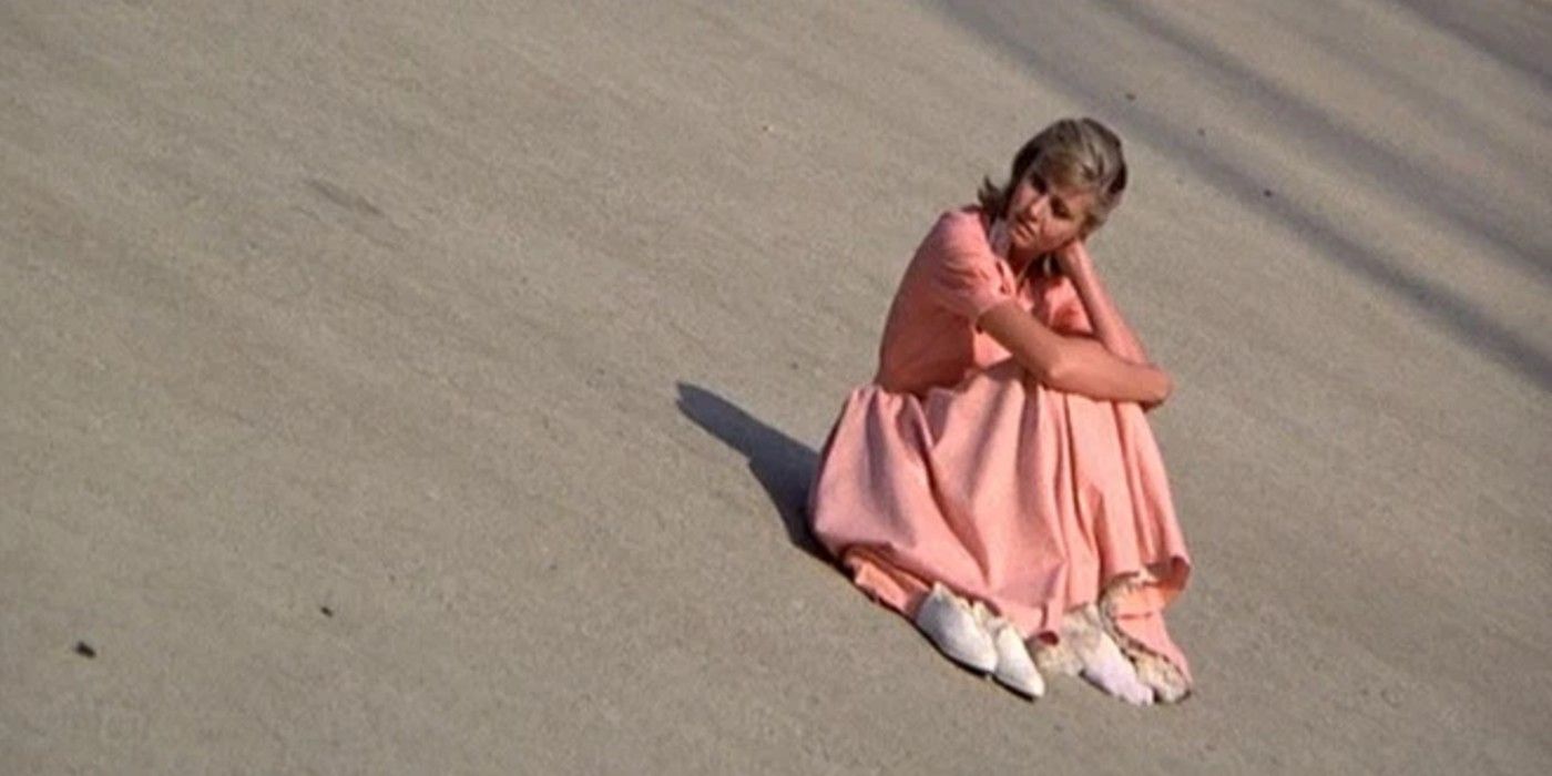 Sandy sitting on the concrete in her pink dress in Grease
