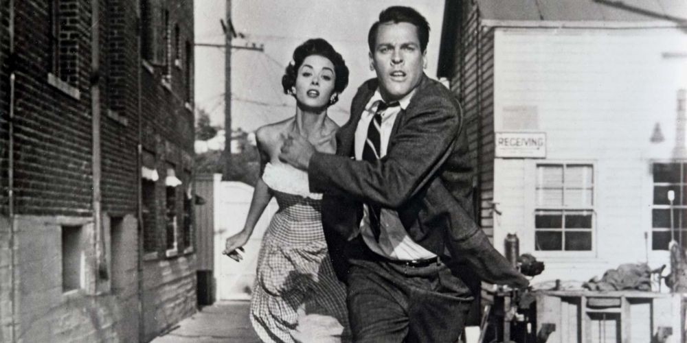 A man and a woman run down a street in Invasion of the Body Snatchers.