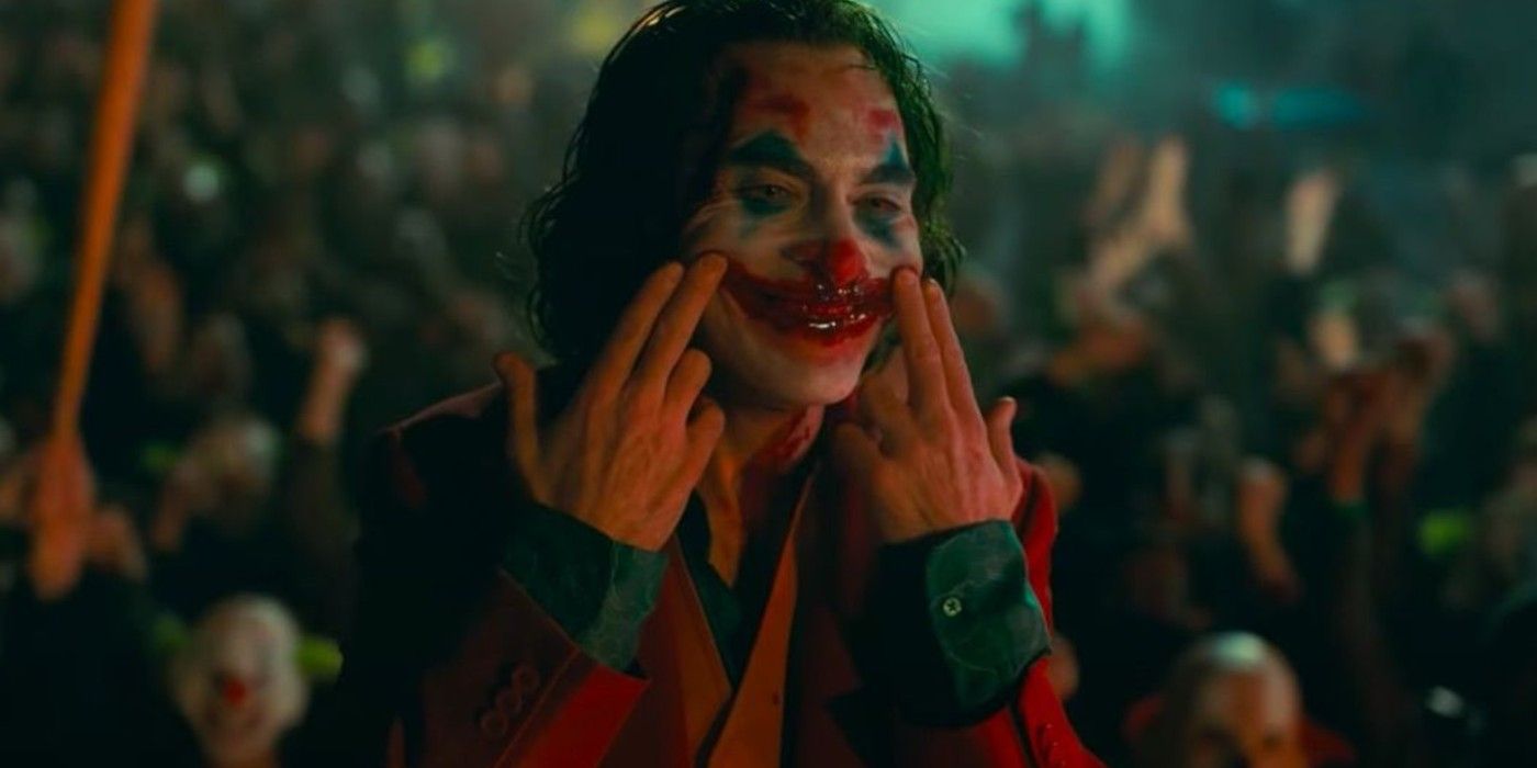 Joker draws a smile in his face using human blood while a riot rages behind him, in Joker