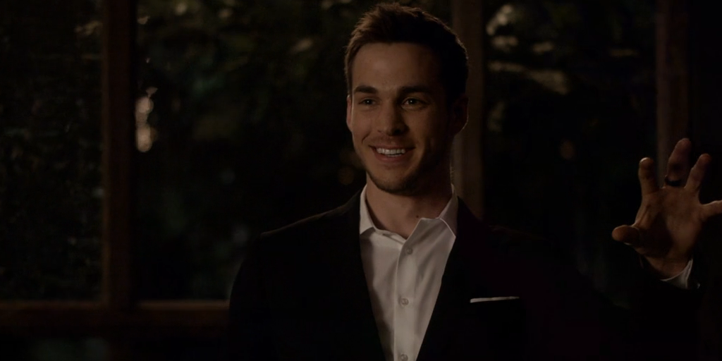 Kai Parker grinning evilly with left open palm up and facing the audience in The Vampire Diaries