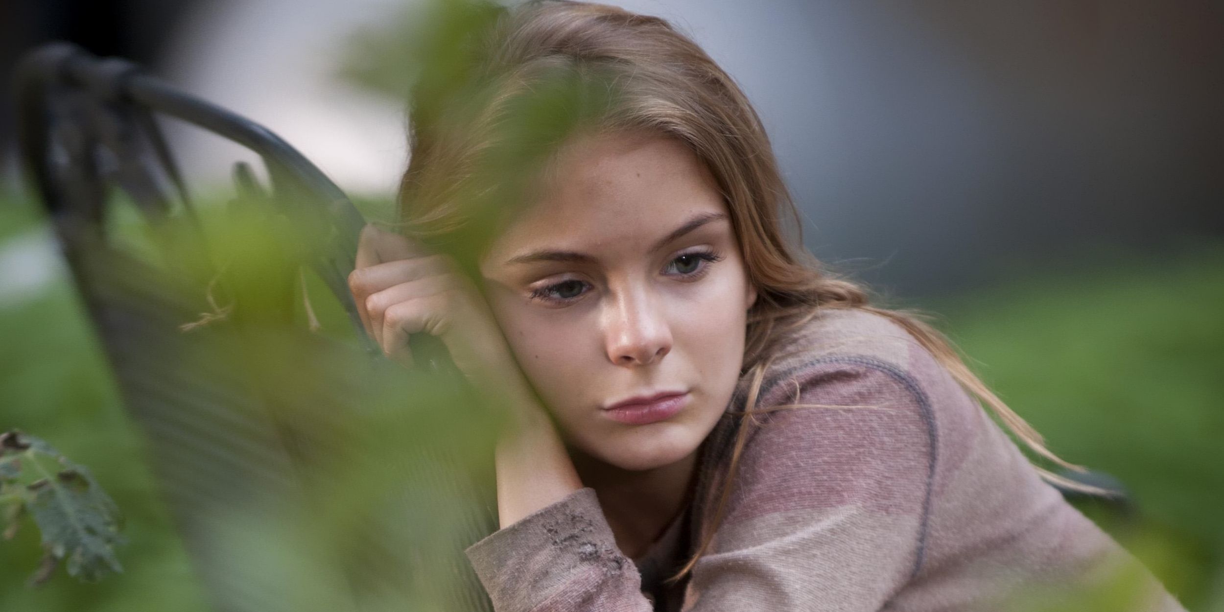 Lizzie Samuels from The Walking Dead leaning against a weapon, looking sad.