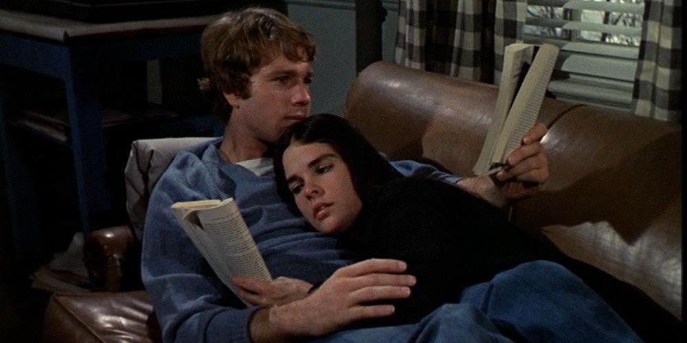 Ryan O'Neal and Ally McGraw lying on the couch together and reading in Love Story
