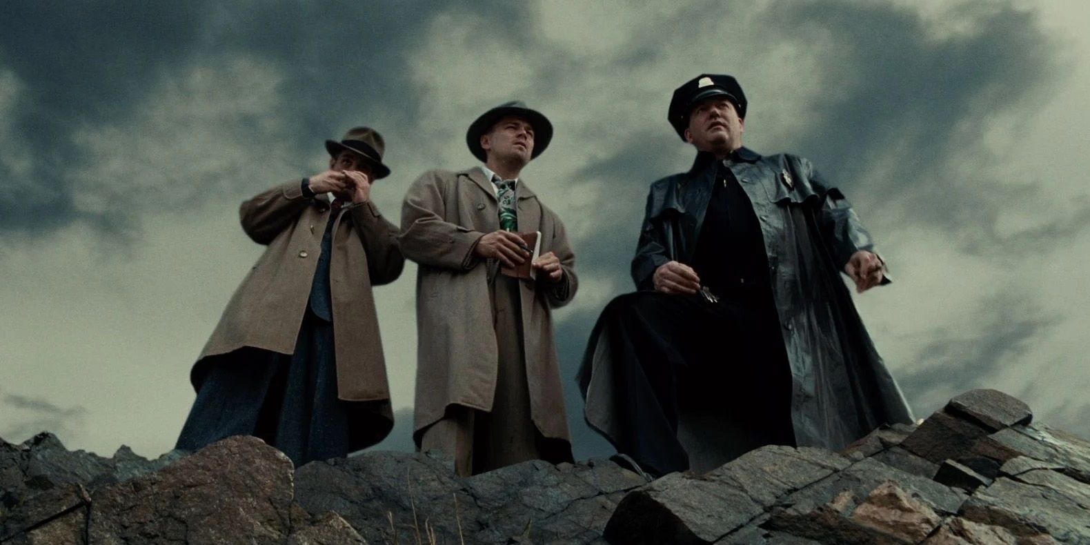 Two detectives and a policeman stand on a cliff in Shutter Island