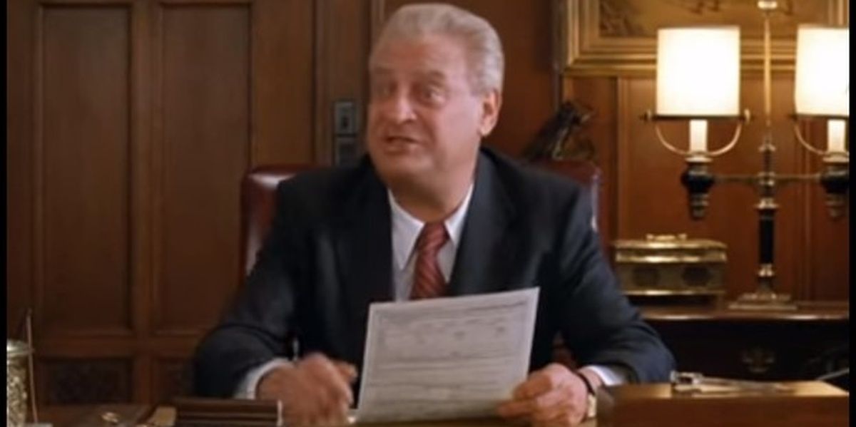 Rodney Dangerfield sitting at a desk, holding an application in Moving