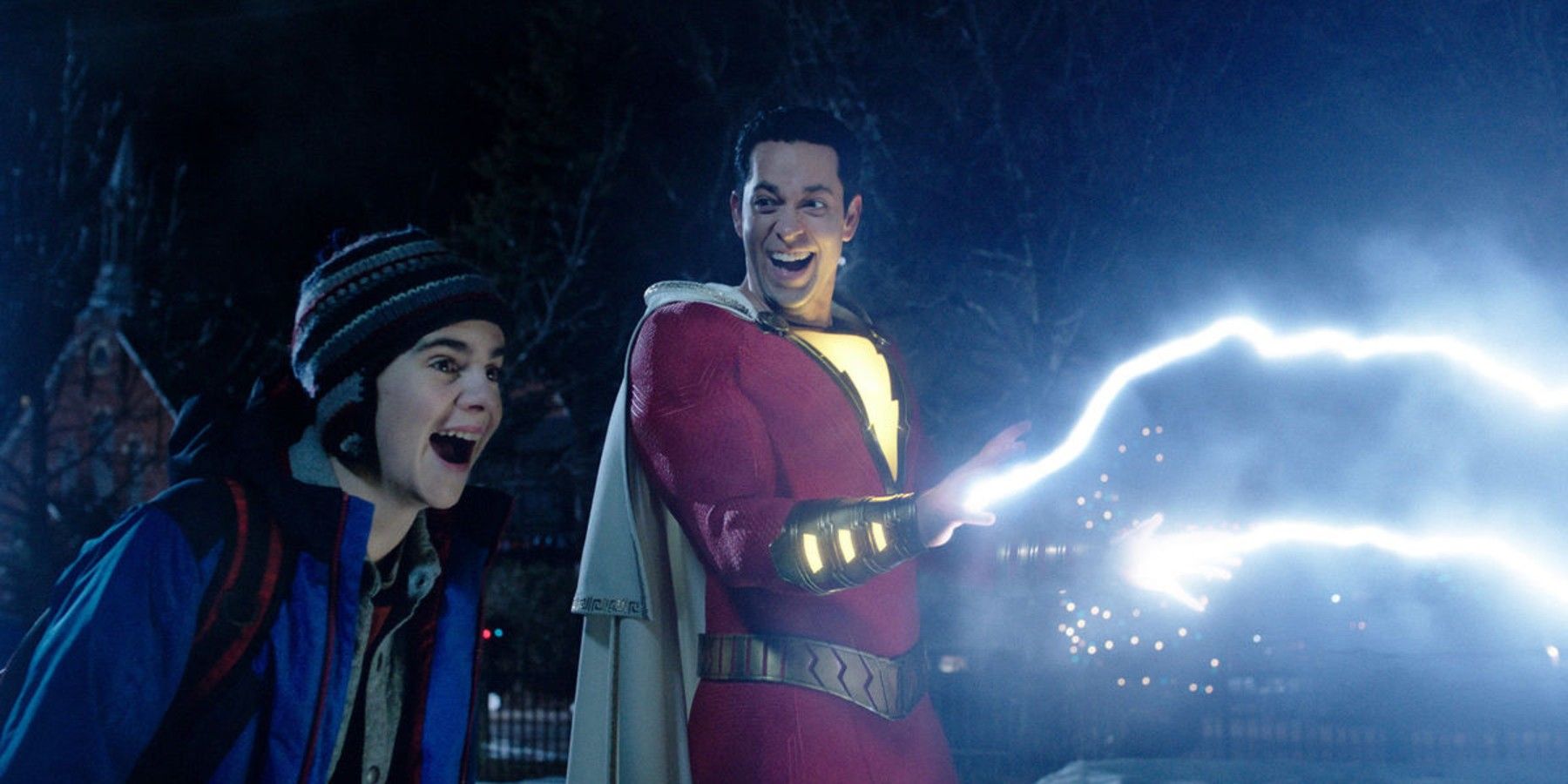 Billy Batson, as Shazam, fires lightning from his hands as he and Freddy Freeman look excited