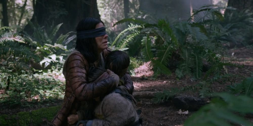 Sandra Bullock holding a child in the woods in Bird Box