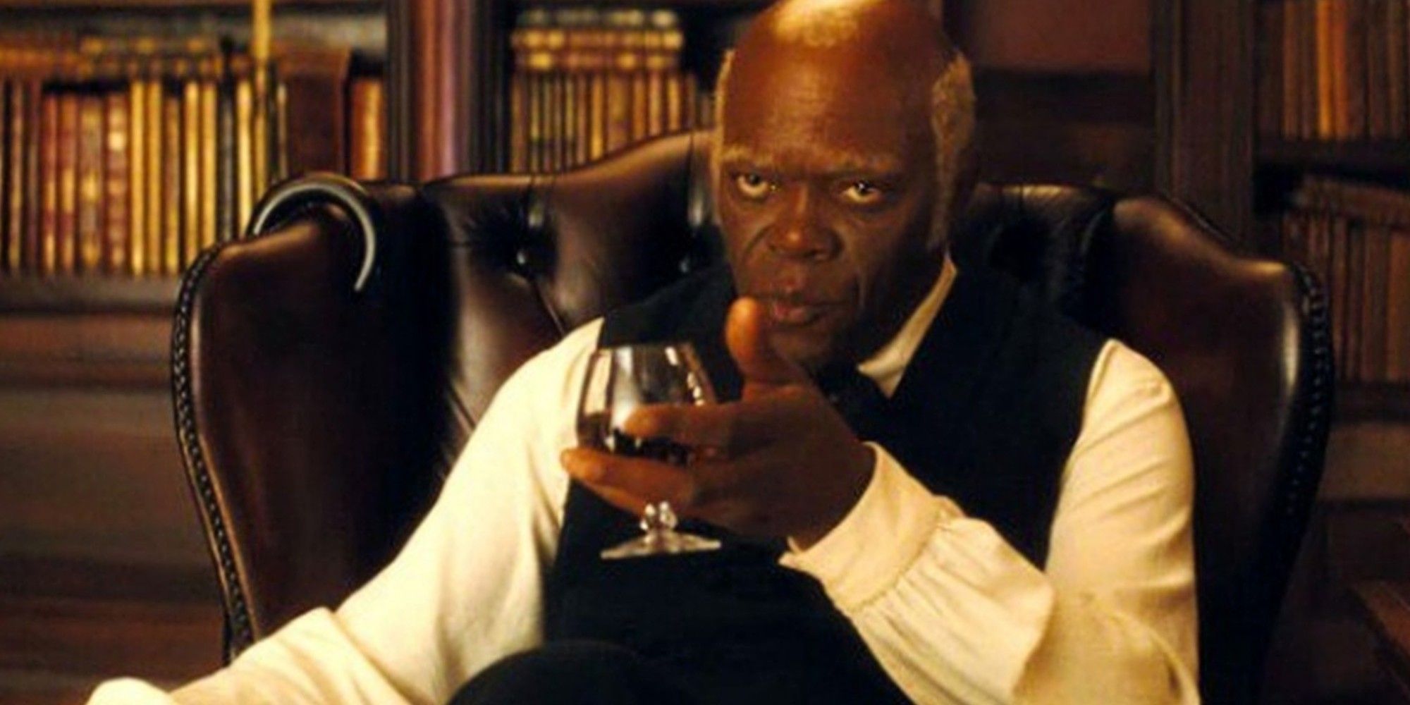 Stephen sitting down and holding a drink in his hand in Django Unchained
