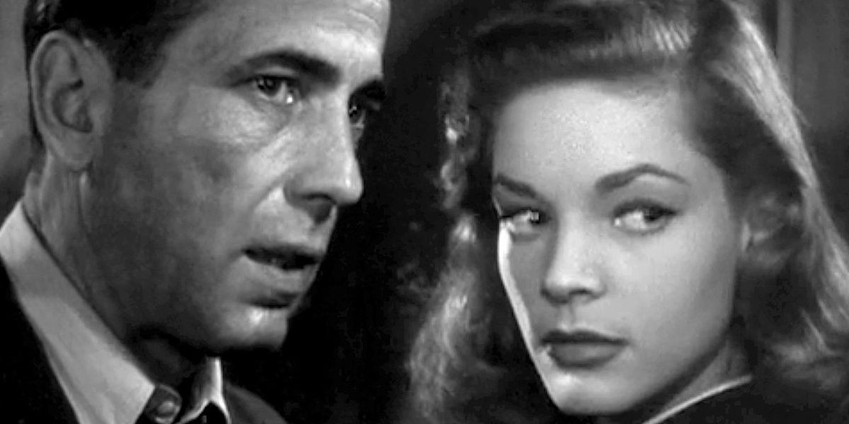 Humphrey Bogart and Lauren Bacall stand closely together and look to the side in The Big Sleep.