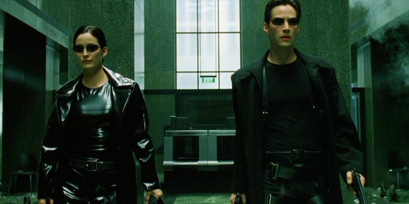 Carrie-Anne Moss as Trinity and Keanu Reeves as Neo walking while extremely well-armed before rescuing Laurence Fishburne as Morpheus in The Matrix
