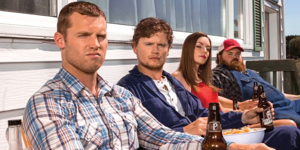 The cast of Letterkenny sitting outside side by side with beers and looking at the camera
