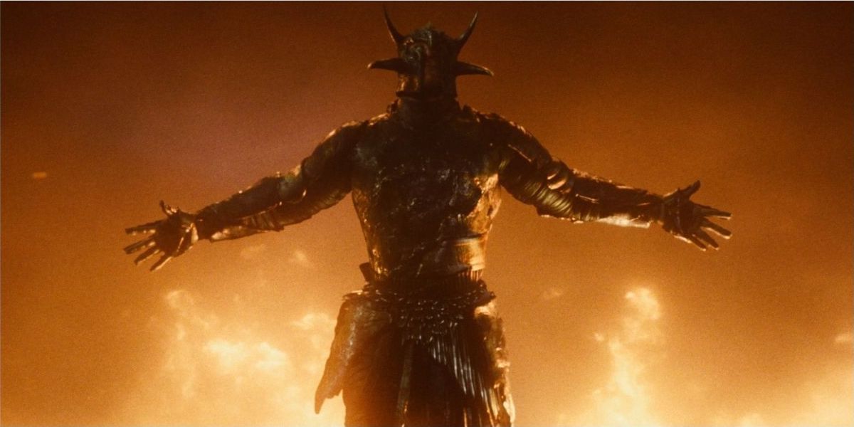 Ares stretches his arms out as fire rages behind him in Wonder Woman.