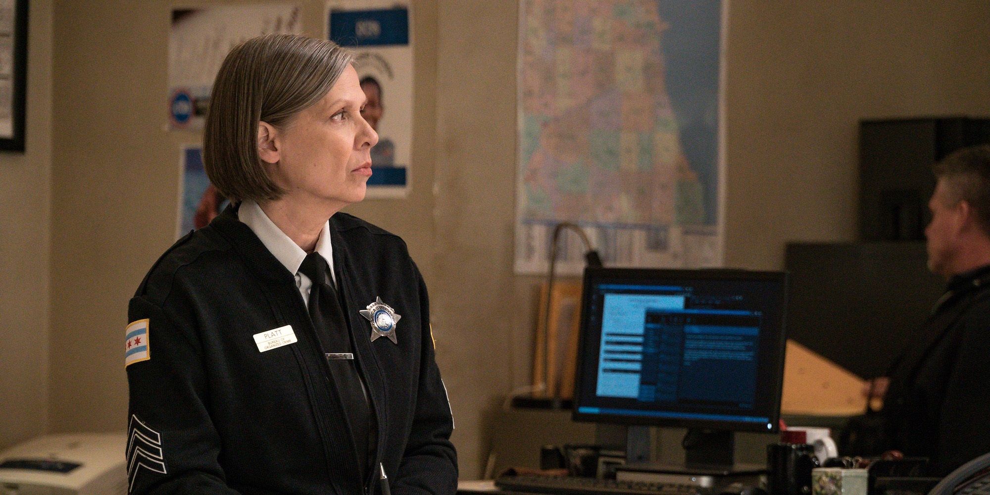 Amy Morton as Trudy Platt standing behind a desk in uniform