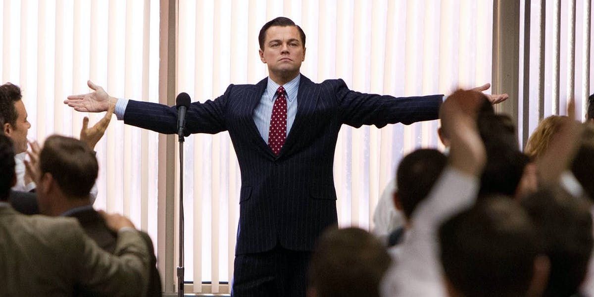 Leonardo DiCaprio as Jordan Belfort raising his arms in front of a group in The Wall of Wall Street 2013