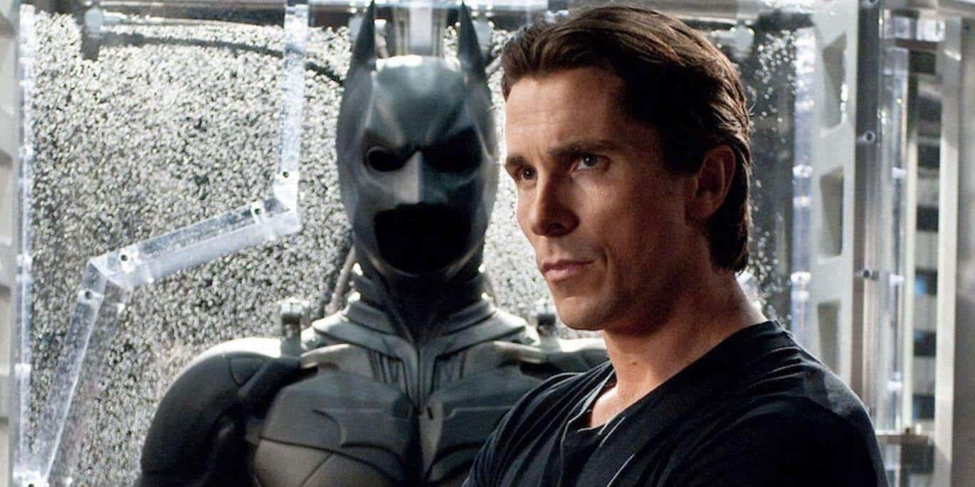 An image of Bruce Wayne standing in front of the Batsuit in Batman Begins