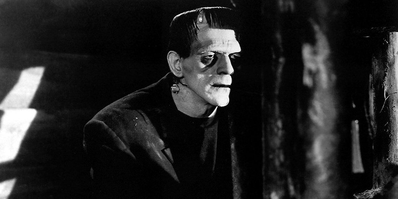 Boris Karloff in Frankenstein (1931) stands in the shadows in a black and white still.
