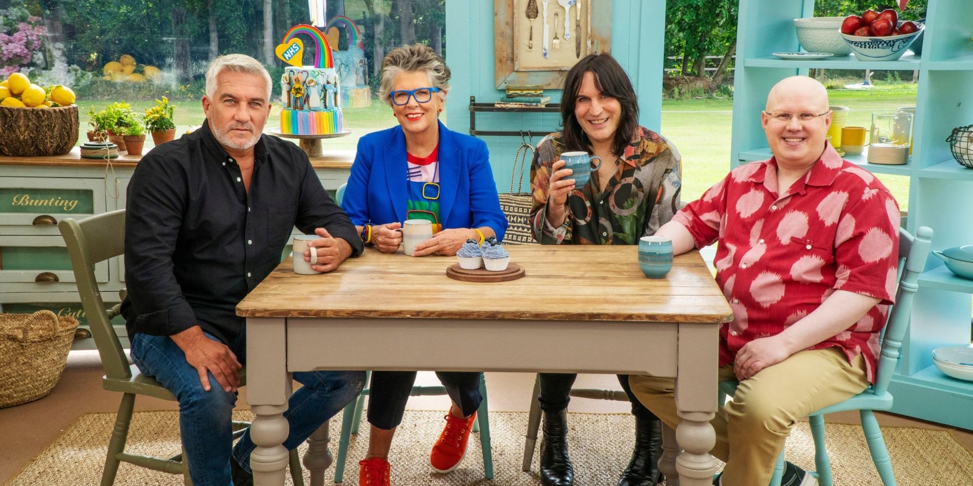 The hosts of The Great British Baking Show sitting at a table