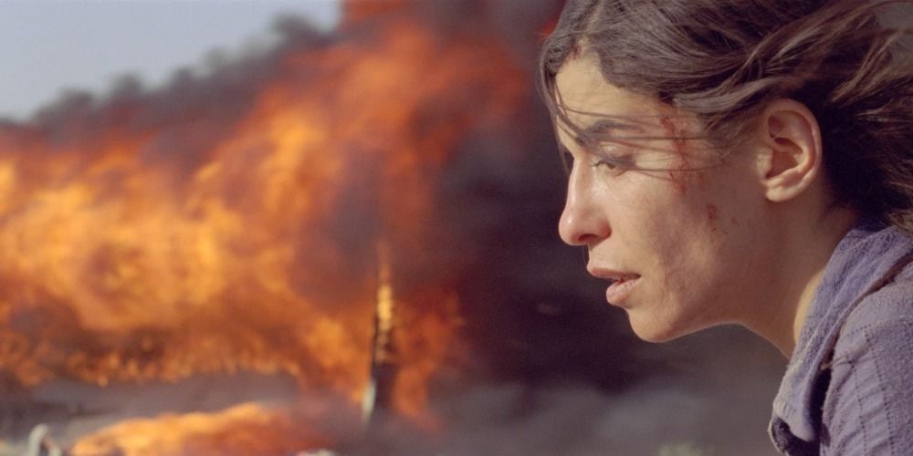 A distressed woman in the foreground and a bus on fire in the background in Incendies.