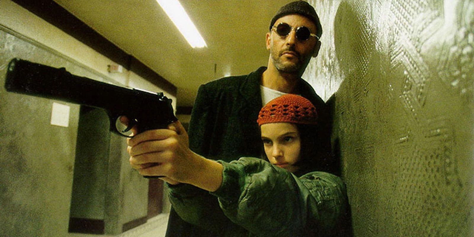 Jean Reno standing behind Natalie Portman pointing a gun in Leon The Professional