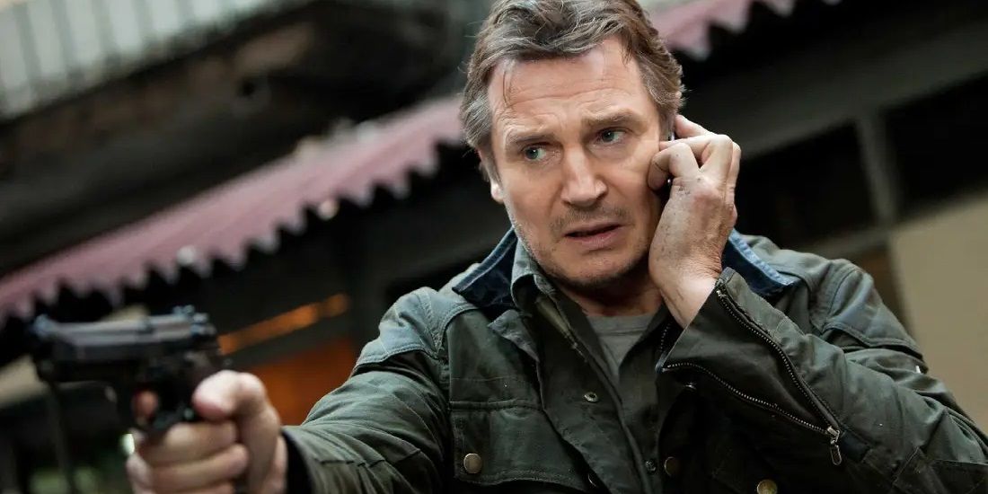Liam Neeson as Bryan Mills on the phone and pointing a gun in Taken 3