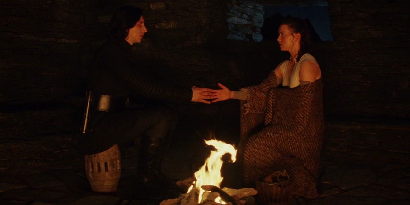 Rey and Kylo Ren touch hands in the hut on Ahch To in Star Wars