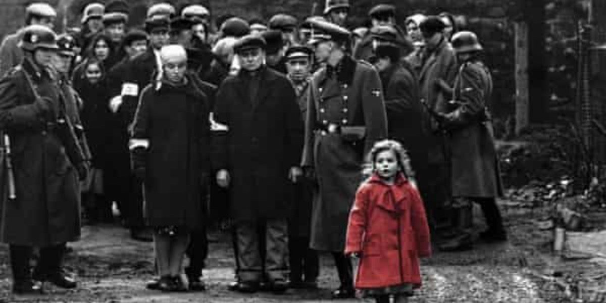 A girl in a red dress stands among a crowd in black and white from Schindler's List