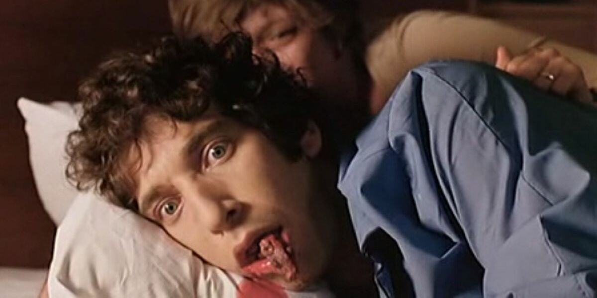 A still from Shivers featuring a man laying on a pillow as a parasite squirms out of his mouth