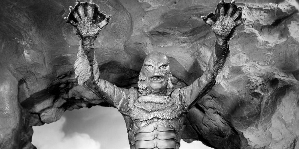 The Gill man raises his arms inside of his lair from Creature from the Black Lagoon