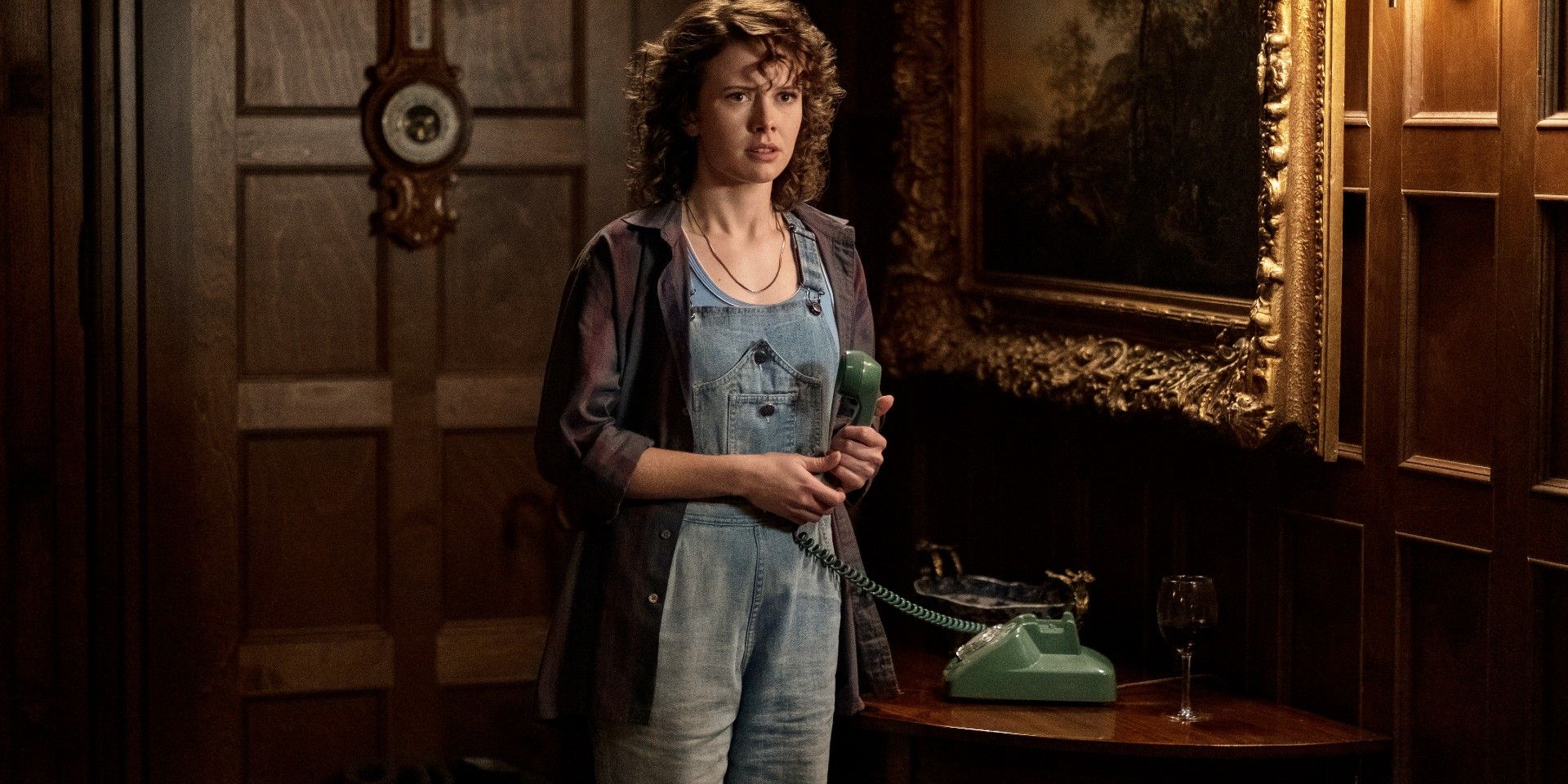 Jamie (Amelia Eve) stands in the halls of Bly Manor, holding the phone and wearing overalls, in The Haunting of Bly Manor