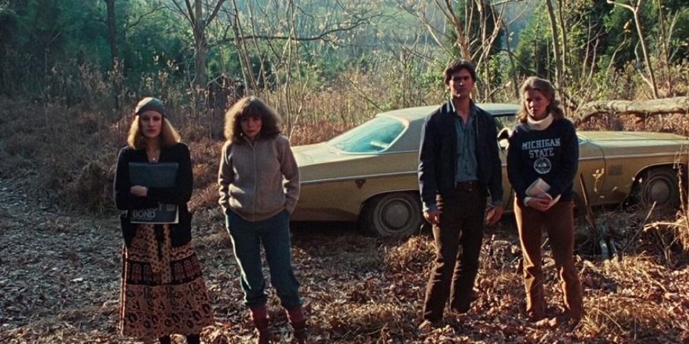 The main characters of The Evil Dead standing by the car and looking toward the camera at the cabin
