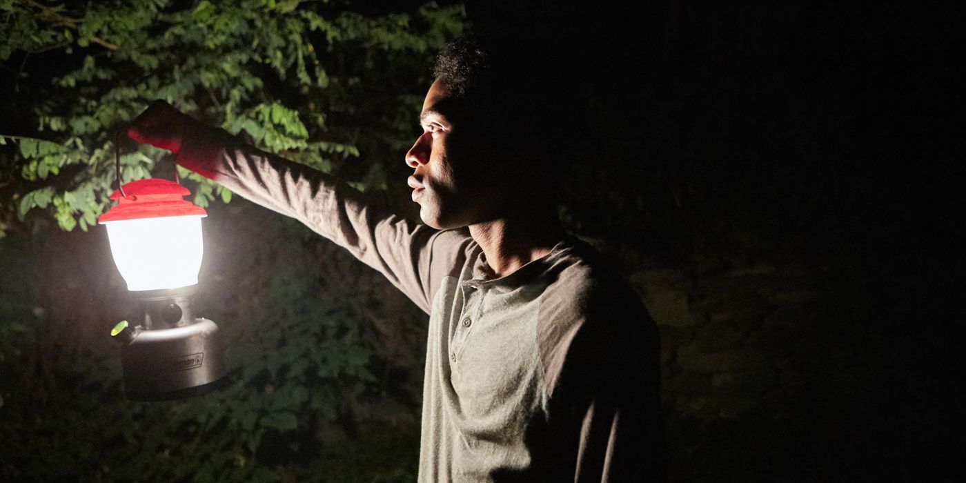 Travis holding a lantern in the woods at night in It Comes at Night
