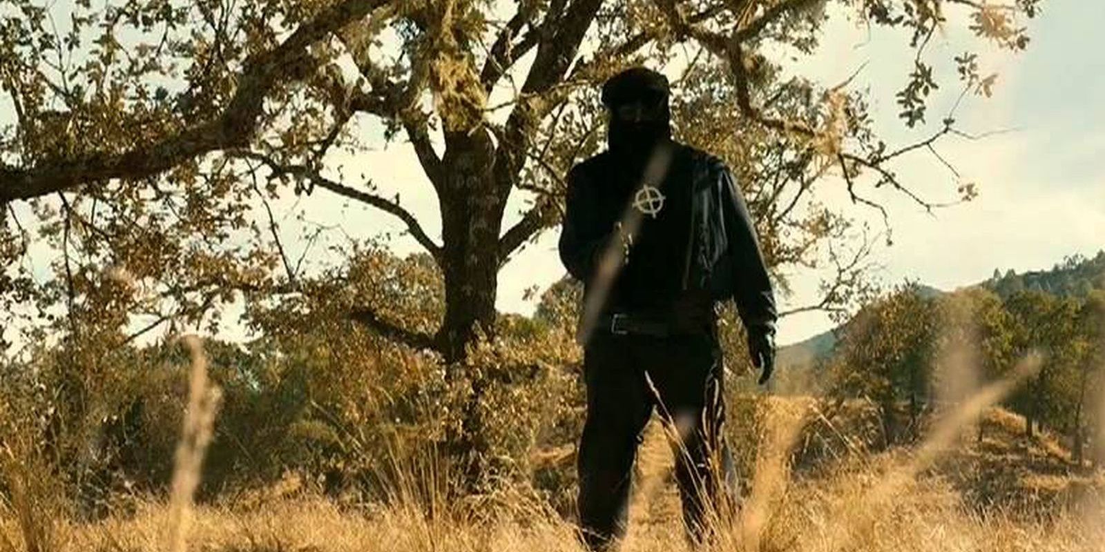 A man clad all in black brandishes a gun in the woods