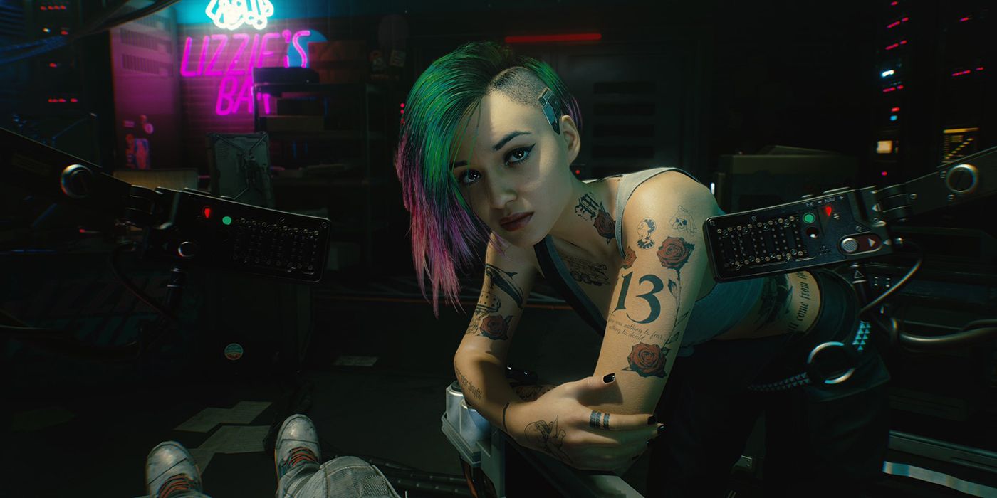 Judy leans on a table and looks at the player character in Cyberpunk 2077.