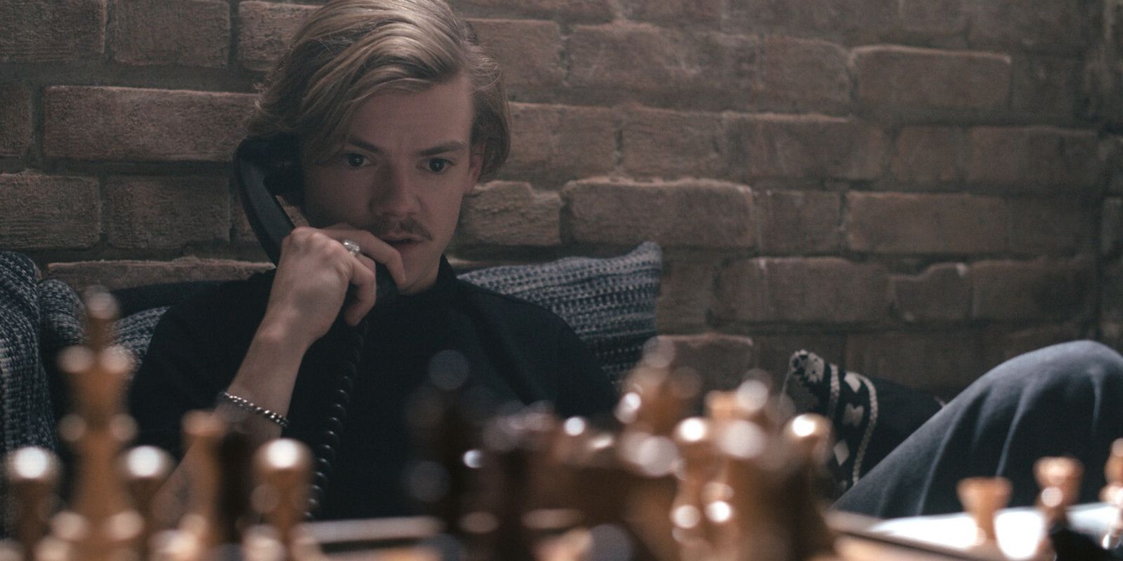 Benny on the phone seated next to a chessboard in The Queen's Gambit